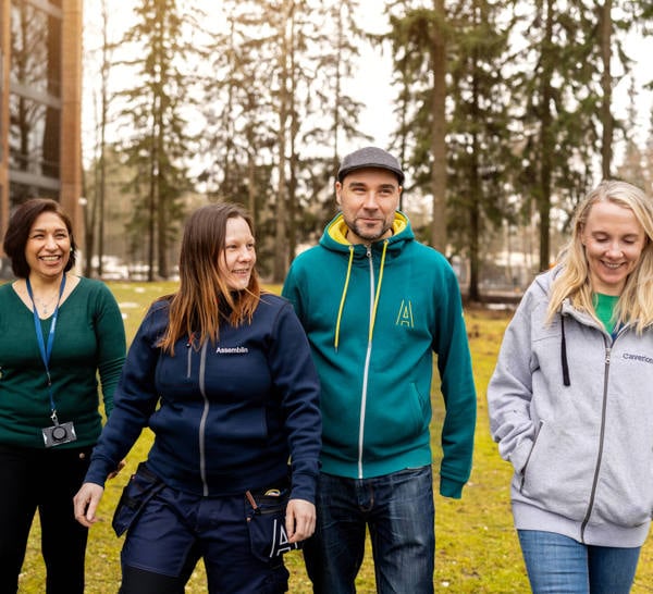 Four people walking towards camera, building and forest in the background