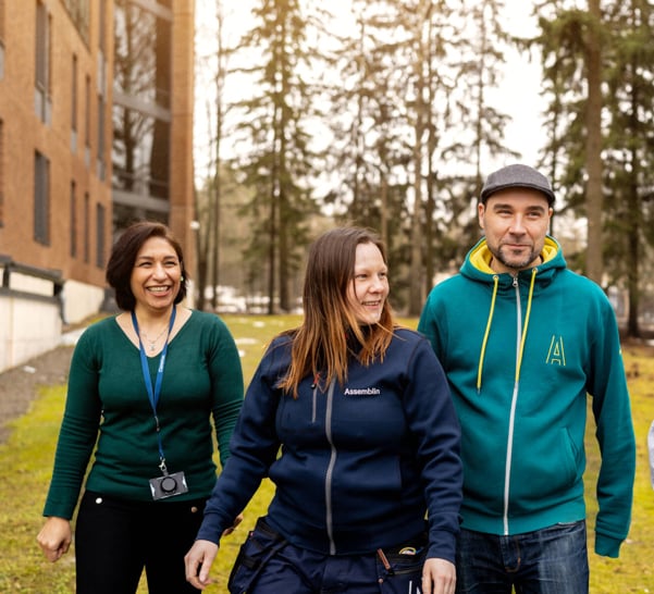 Four people walking towards camera, building and forest in the background